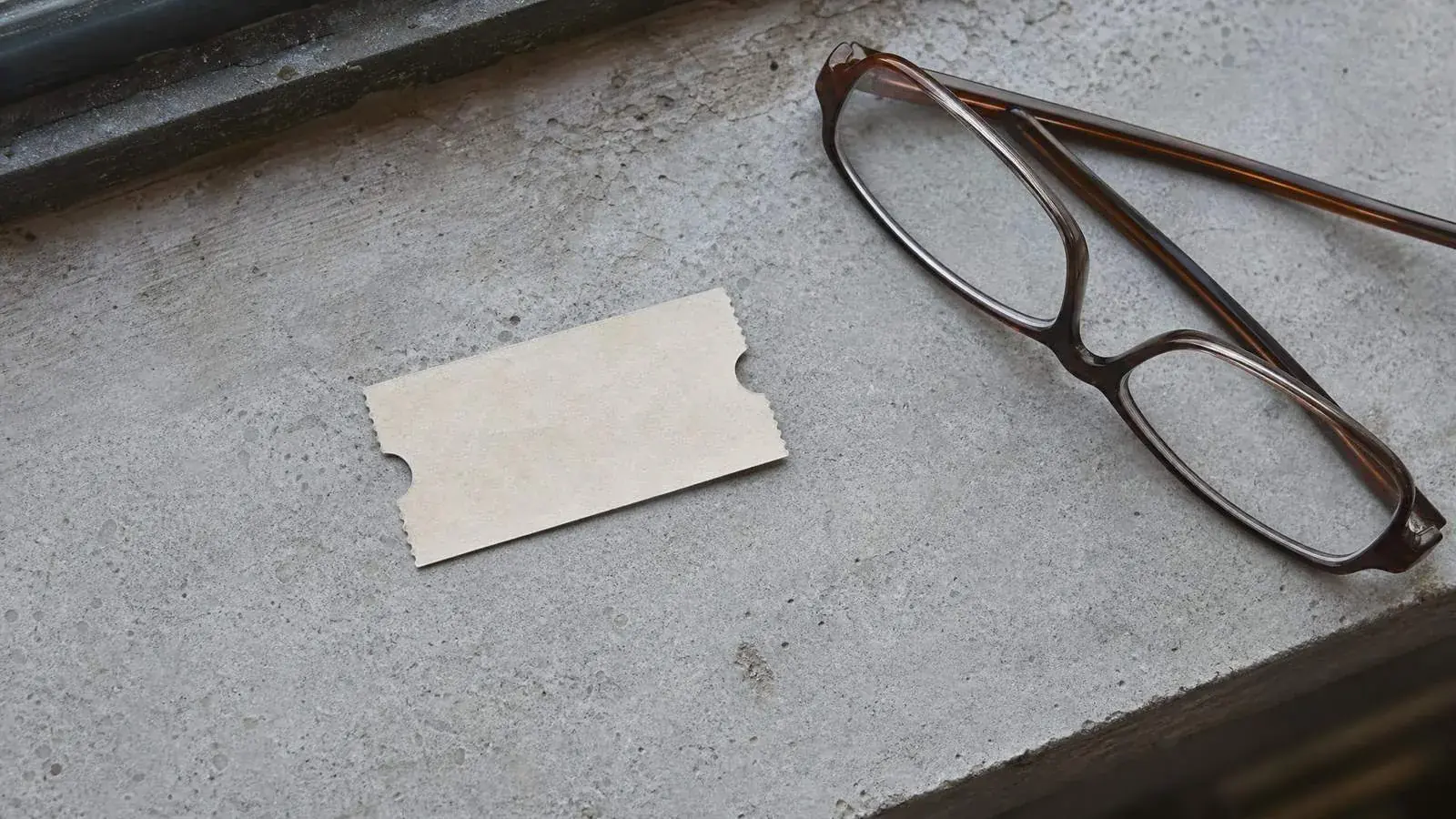 Ein leerer Papier-Eintrittsschein auf einer abgenutzten Steinbank neben einer Lesebrille