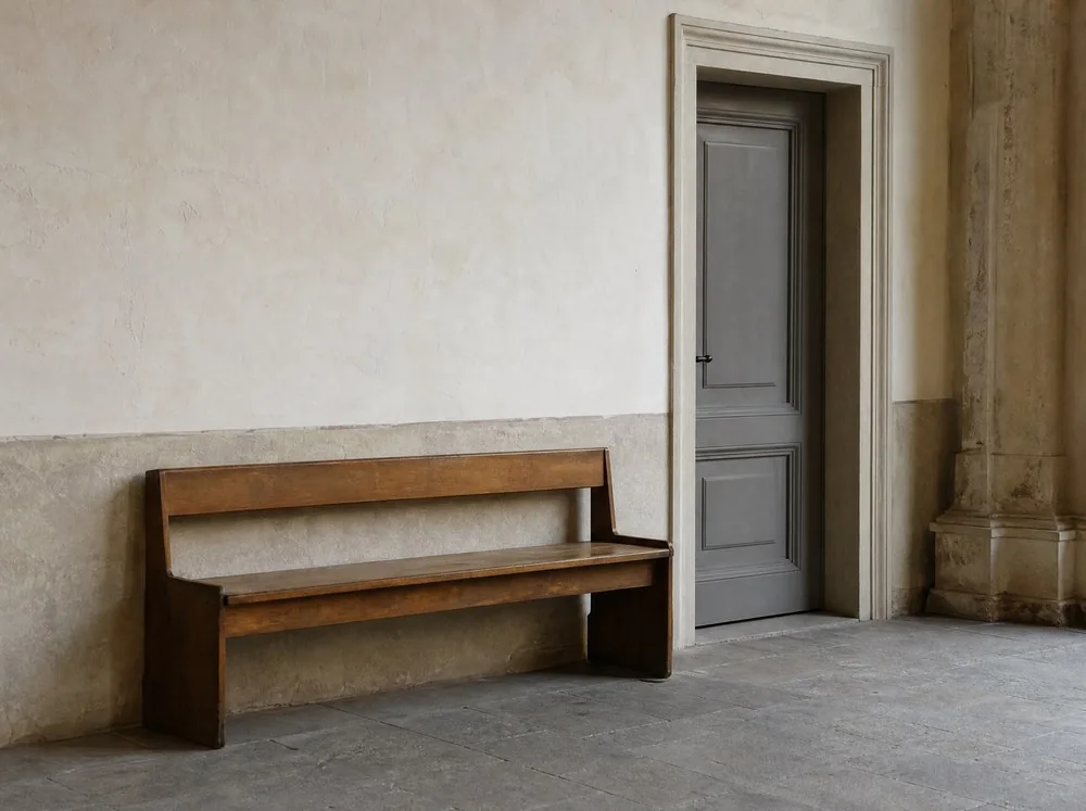 Eine leere Holzbank an einer verputzten Wand neben einer geschlossenen Tür