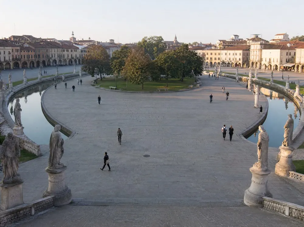 A large oval public square ringed by a water channel and stone statues on plinths