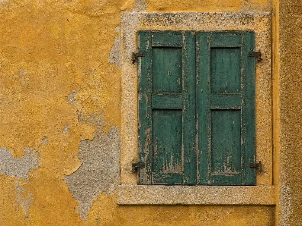 Verwitterte grüne Fensterläden vor einer ockerfarbenen Wand